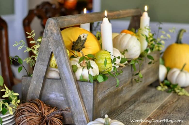 Fall dining room table centerpiece with pumpkins in a wooden box and candles.