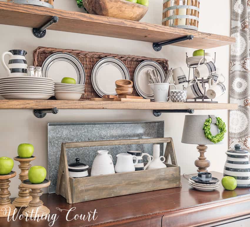 Open rustic farmhouse kitchen shelves decorated with apples and plates. decorated for late summer