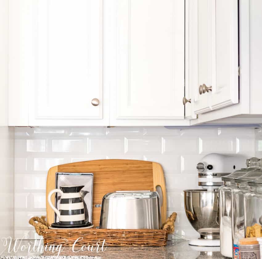 A bread basket with a toaster and pitcher in it on the kitchen counter.