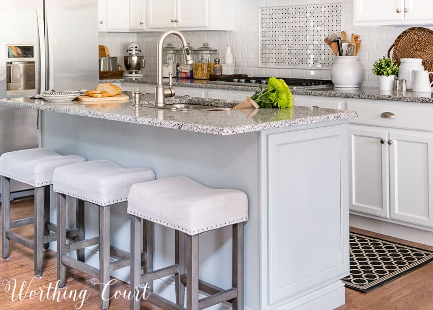 Gray island with white kitchen cabinets with stools around it.