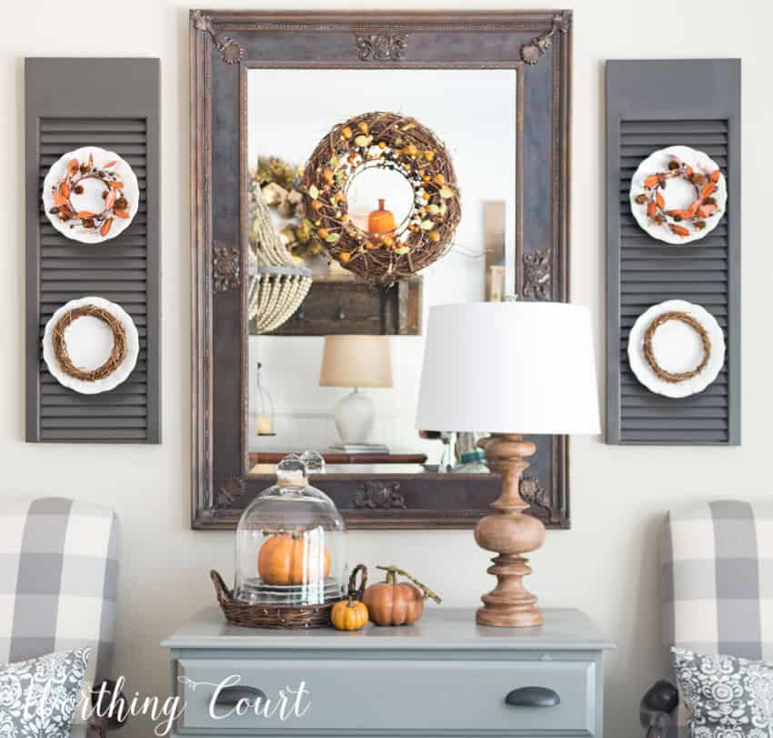 Fall dining room mirror and shutters with plates that have fall decor.