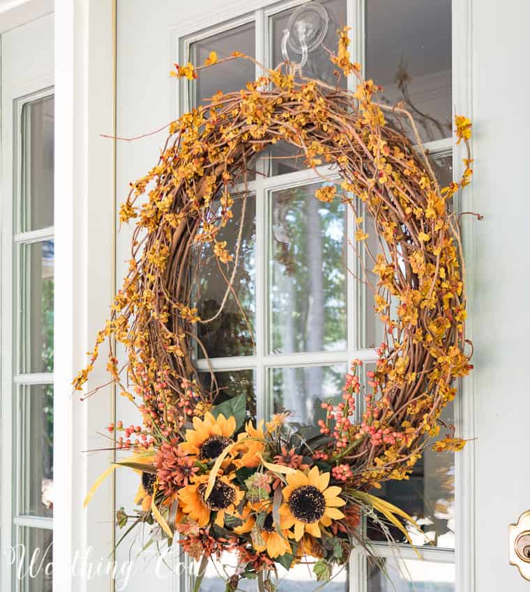 Grapevine wreath decorated for fall with berries and sunflowers.