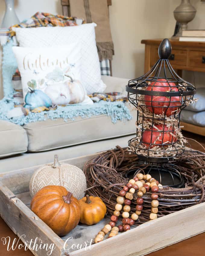 Fall coffee table vignette with orange and white pumpkins and a large twig wreath in a wooden tray on the coffee table.