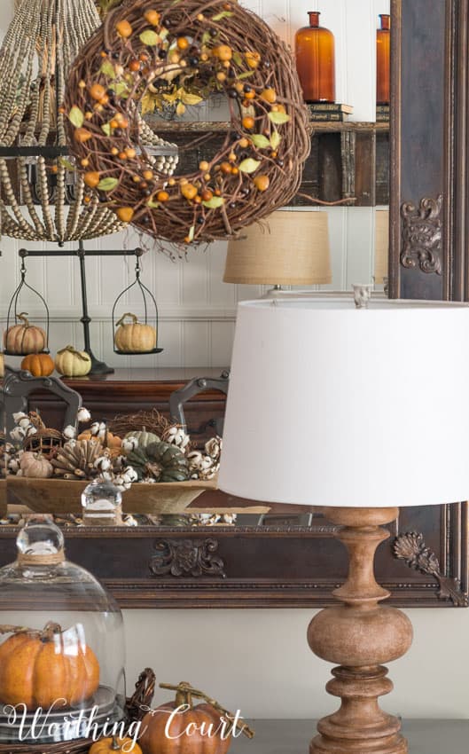 Fall decor reflected in a mirror with a grapevine wreath on it.