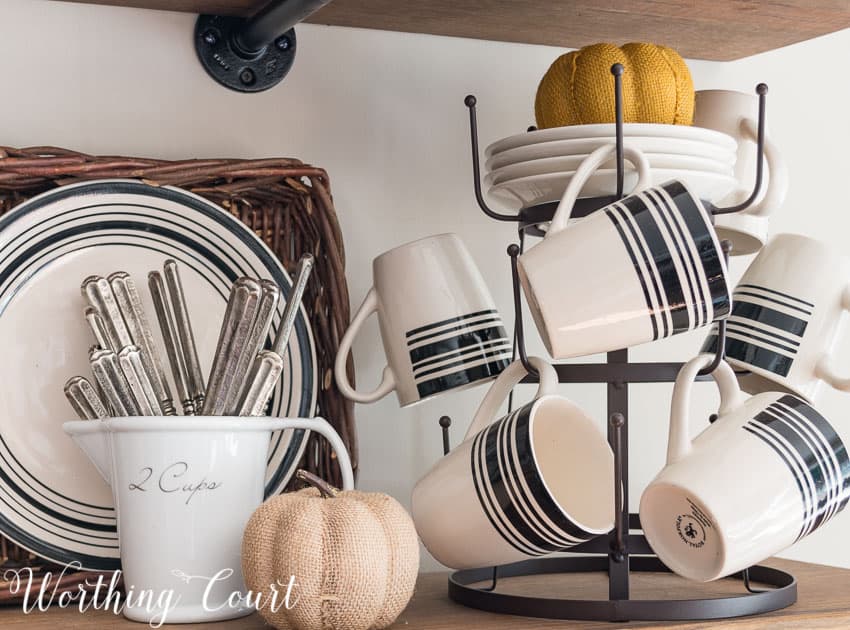 There is a orange fabric pumpkin on plates and a neutral fabric pumpkin beside the cups on the shelving unit.