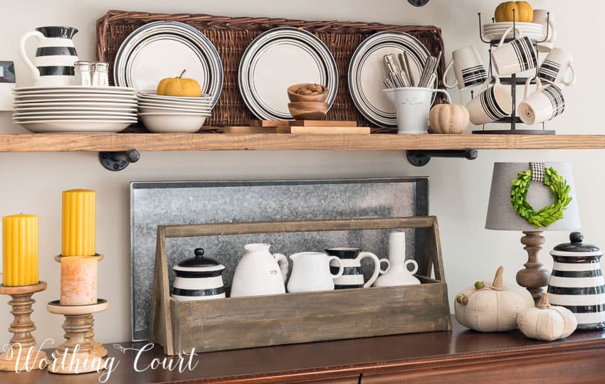 The rustic shelves have a wooden toolbox, black and white striped dishes and pitcher and also yellow candles.