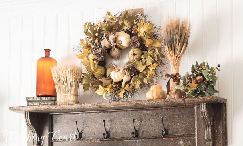 A wooden mantel shelf with a fall wreath above it, and amber glass on the shelf.