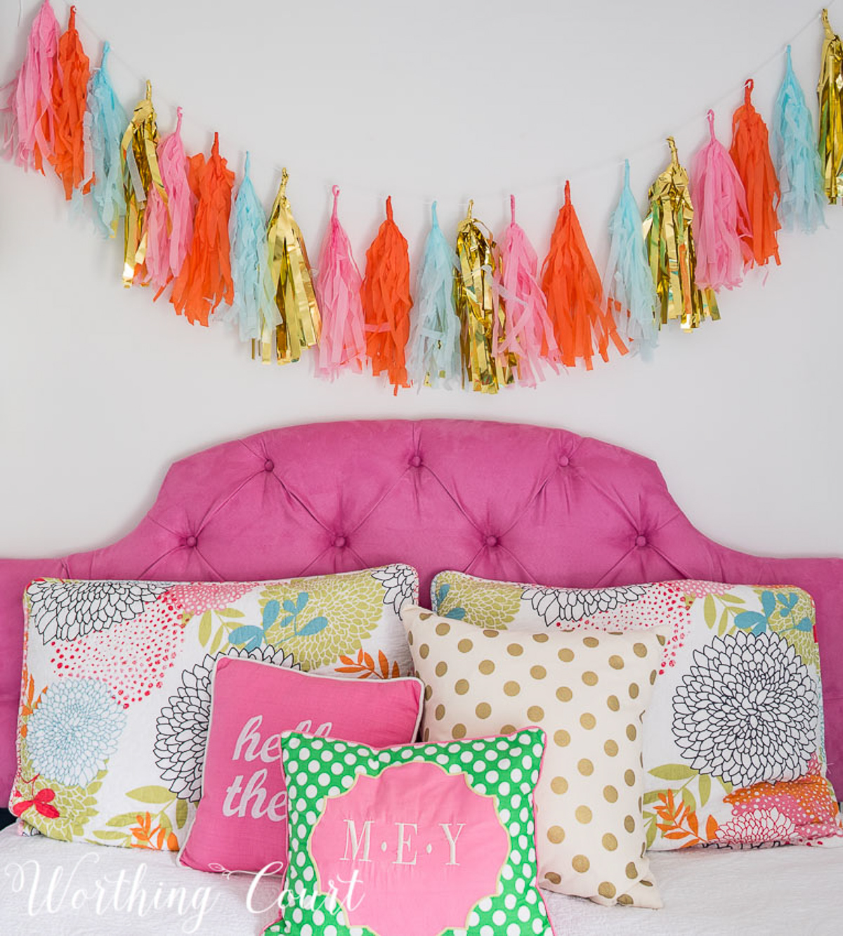 colorful teenage girls bedroom with a pink headboard, furniture painted white, teal lamp shades, teal throw, brass trunk, tissue paper garland and a gallery wall