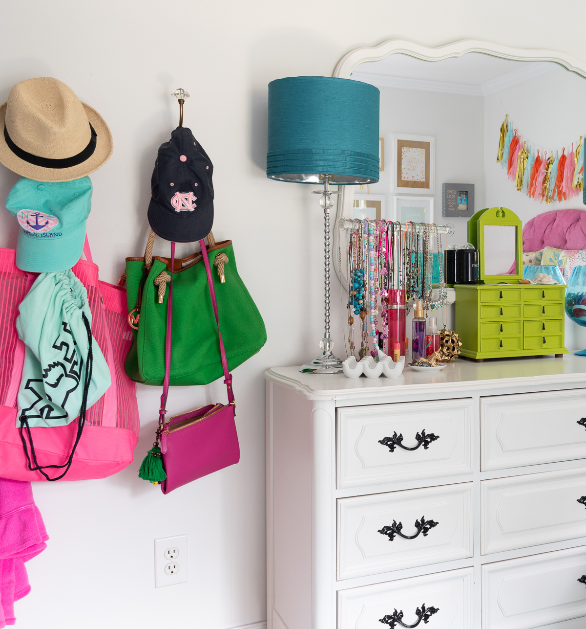 colorful teenage girls bedroom with a pink headboard, furniture painted white, teal lamp shades, teal throw, brass trunk, tissue paper garland and a gallery wall