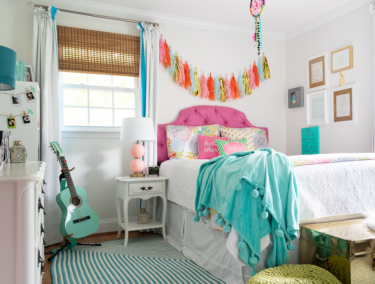 colorful teenage girls bedroom with a pink headboard, furniture painted white, teal lamp shades, teal throw, brass trunk, tissue paper garland and a gallery wall