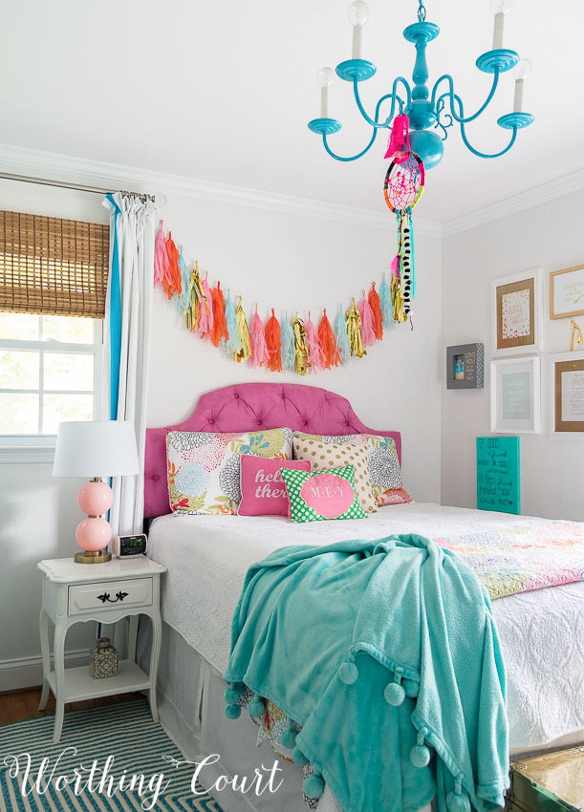 colorful teenage girls bedroom with a pink headboard, furniture painted white, teal lamp shades, teal throw, brass trunk, tissue paper garland and a gallery wall