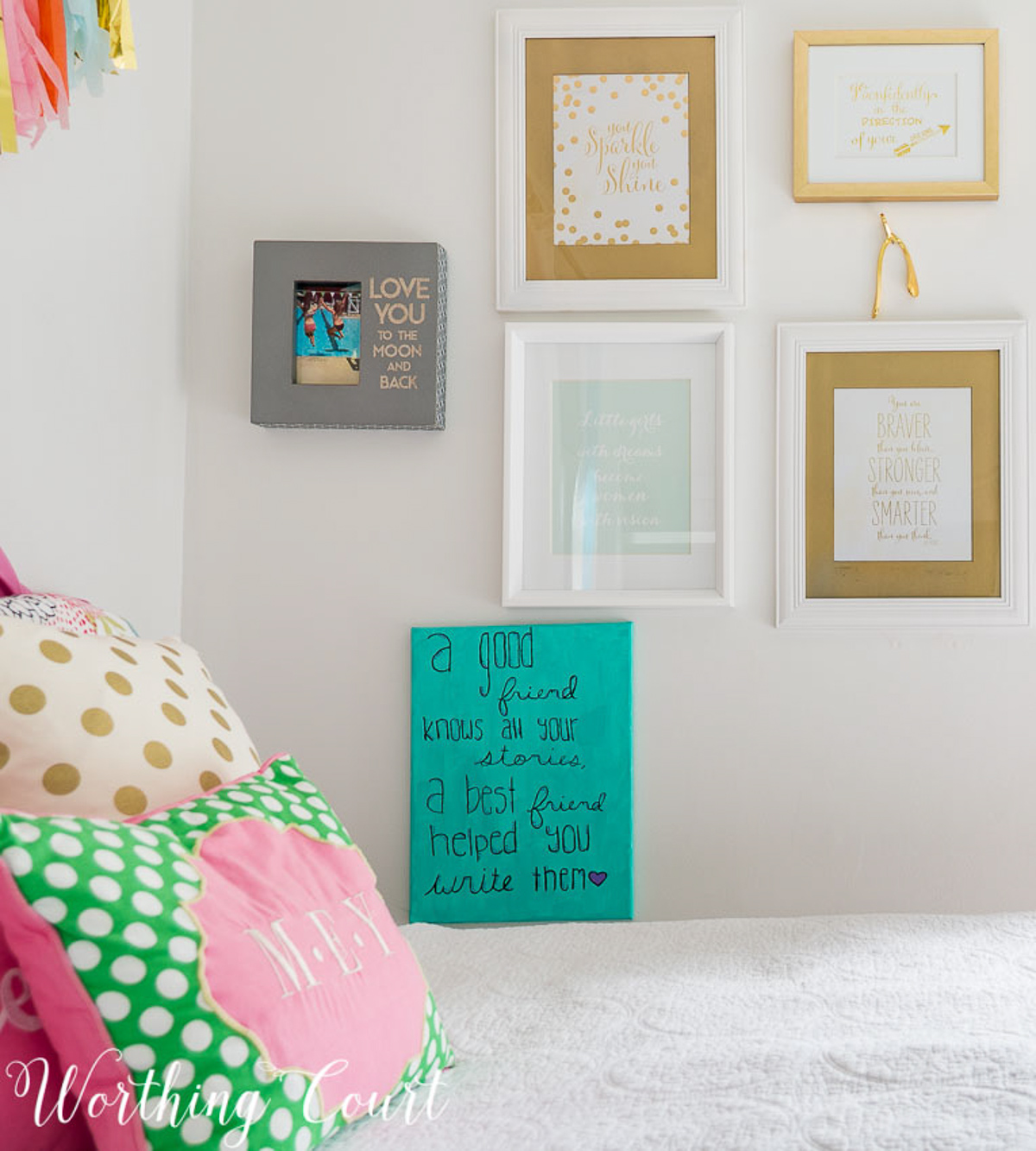 colorful teenage girls bedroom with a pink headboard, furniture painted white, teal lamp shades, teal throw, brass trunk, tissue paper garland and a gallery wall