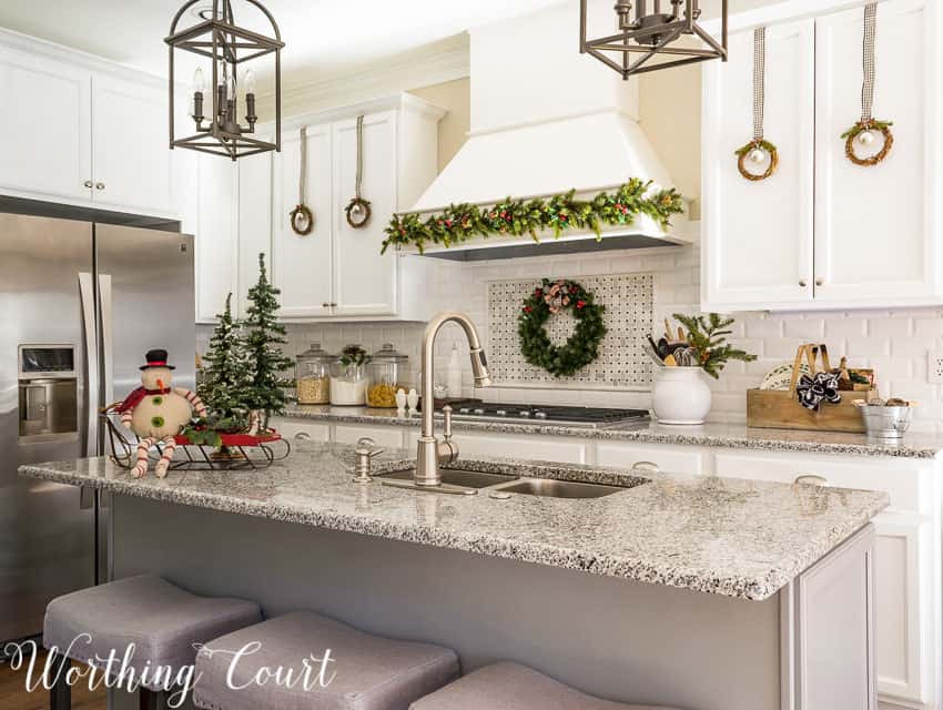 Farmhouse Christmas kitchen with a wreath hanging behind the stove.  There are also twig wreaths hanging on the cupboards.