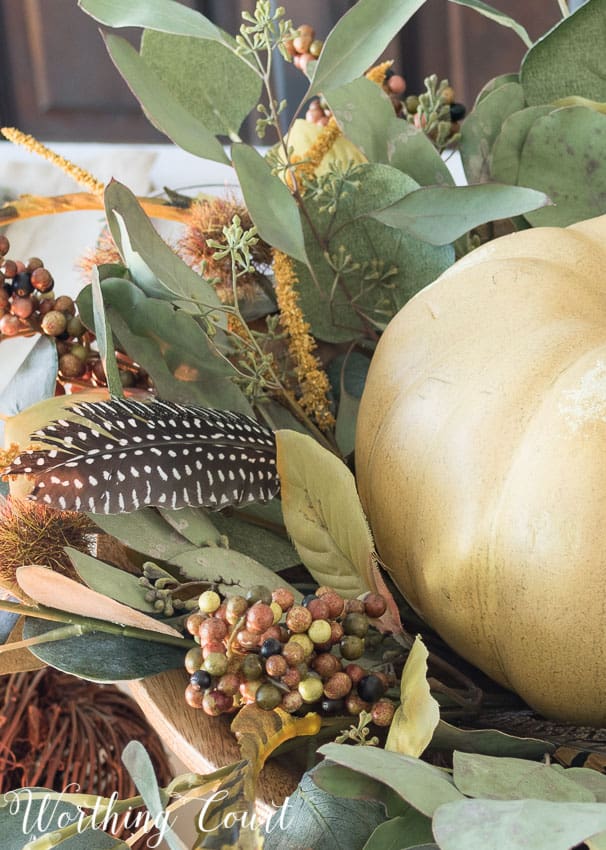 snippet of fall centerpiece with eucalyptus leaves, feathers, berries and a white pumpkin