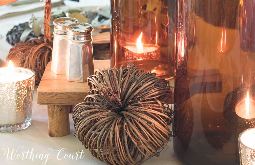 snippet of a fall centerpiece using amber bottles, vine pumpkins and mercury glass