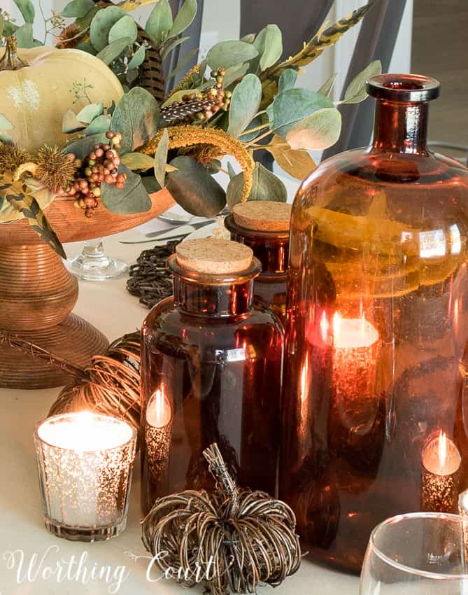 thanksgiving centerpiece with eucalyptus, amber bottles and mercury glass votives