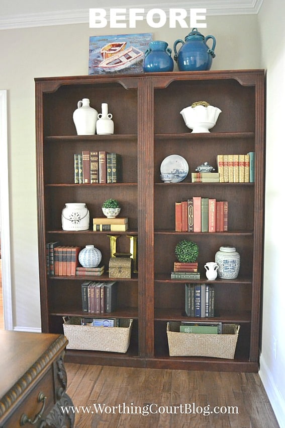 A traditional cherry bookcase in the office with books and pottery on it.