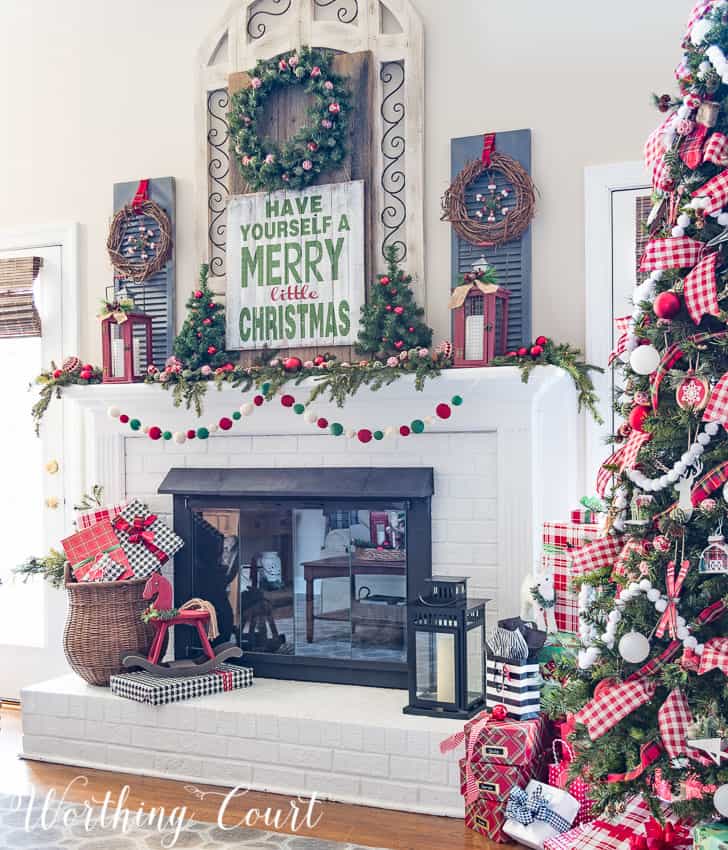 Farmhouse Christmas mantel decorated with traditional red and green with a large decorated Christmas tree beside it.