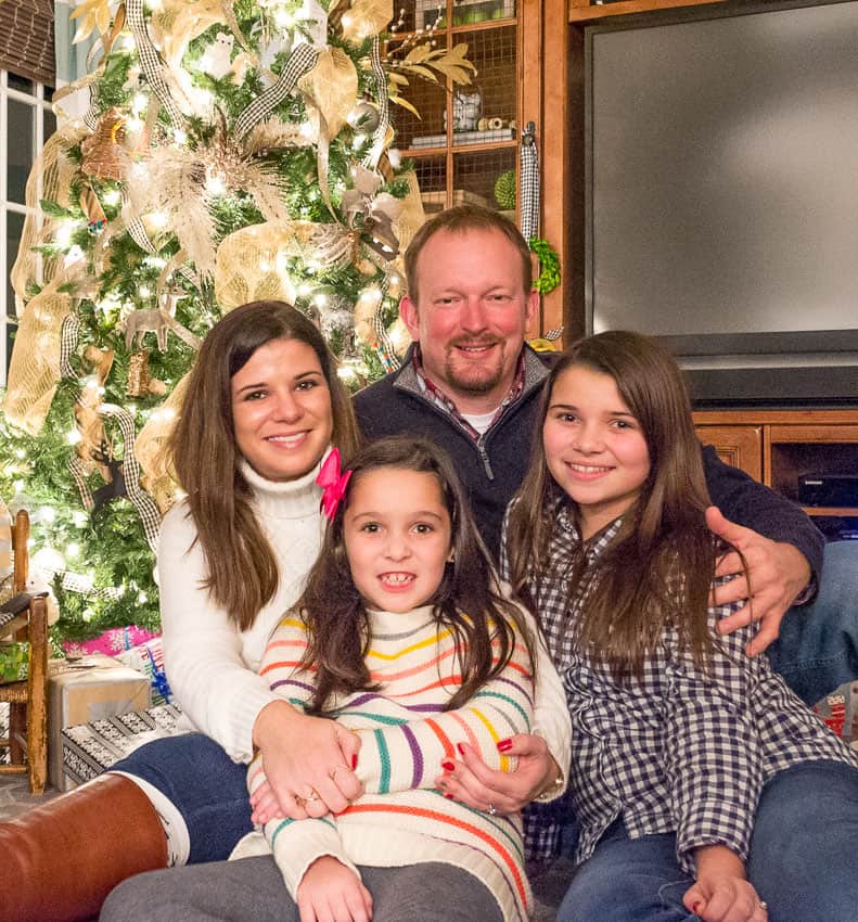 A picture of a Mom and Dad with their two children in front of a Christmas tree.