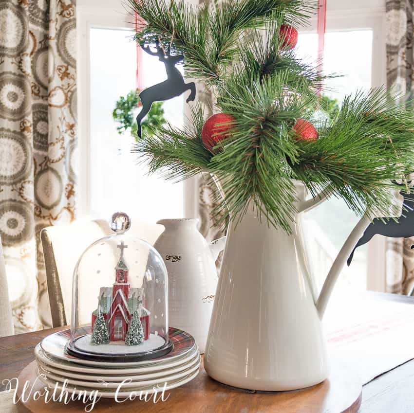 Farmhouse kitchen table Christmas centerpiece with a glass cloche and a white vase with greenery.