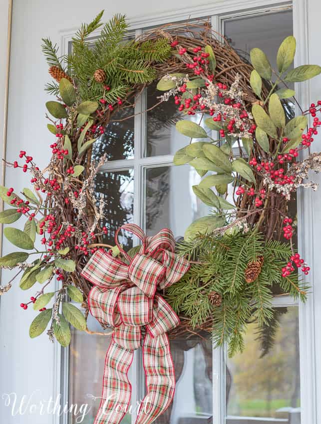 DIY grapevine Christmas wreath with red berries and a plaid bow.