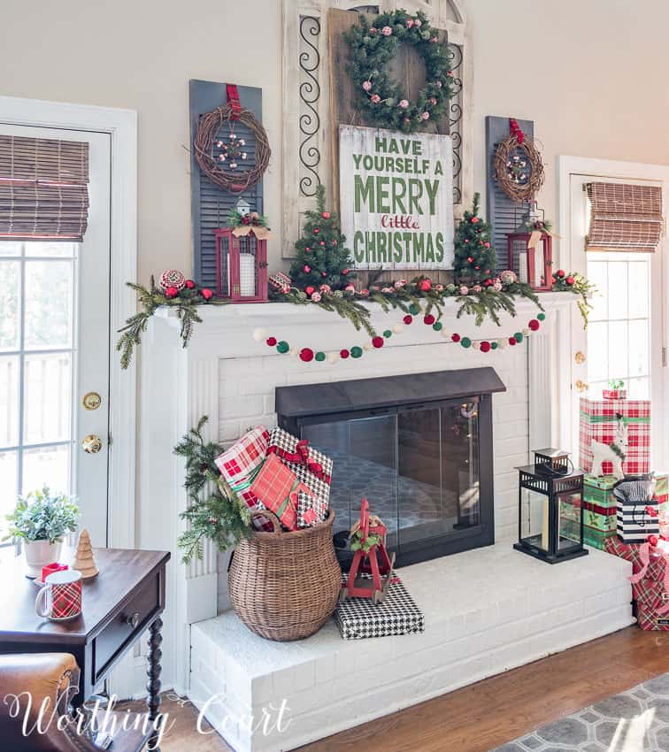 There is a large wicker basket filled with presents on the white fireplace mantel.