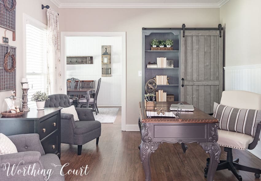 A home office with a grey desk and fabric chair, and a farmhouse style bookcase.