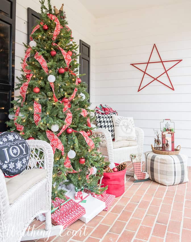 Front porch Christmas tree with red and white ribbon on it.