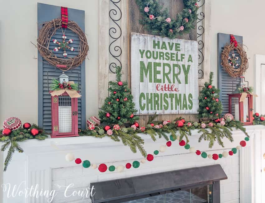 Grapevine wreaths, mini Christmas trees and decorative window shutters are on the mantel.