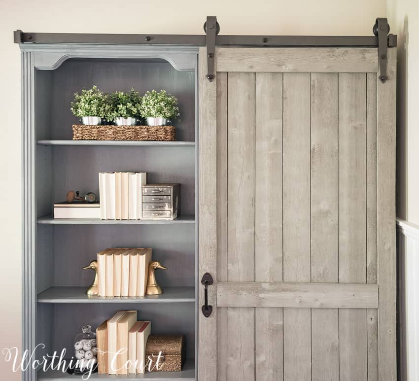 The open shelves on the bookcase with plants and books on them.