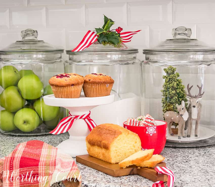 There are green apples in a glass canister beside the home made loaf.