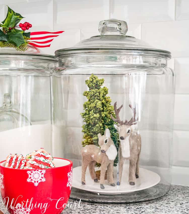 Christmas vignette in a glass canister of deer and a Christmas tree.
