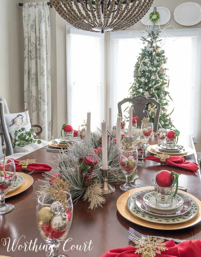 A red, and gold tablescape with white candles and large tree at the foot of the dining room table.