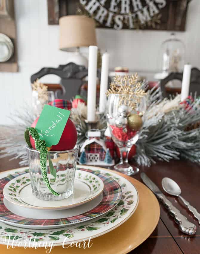 Christmas dinner place setting with gold charger, gold rimmed holly dishes and tartan plaid dishes. 