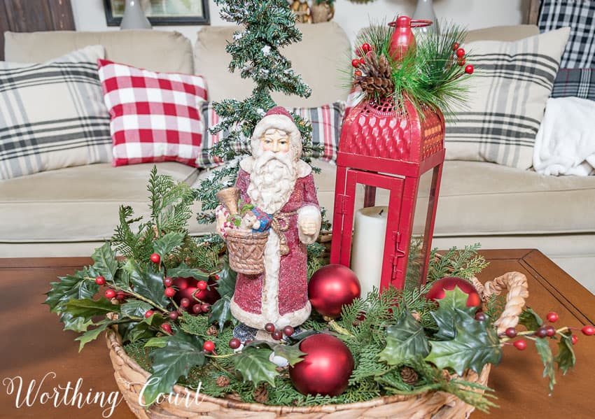 There is a Santa figurine next to ornaments and faux greenery in the round vignette.