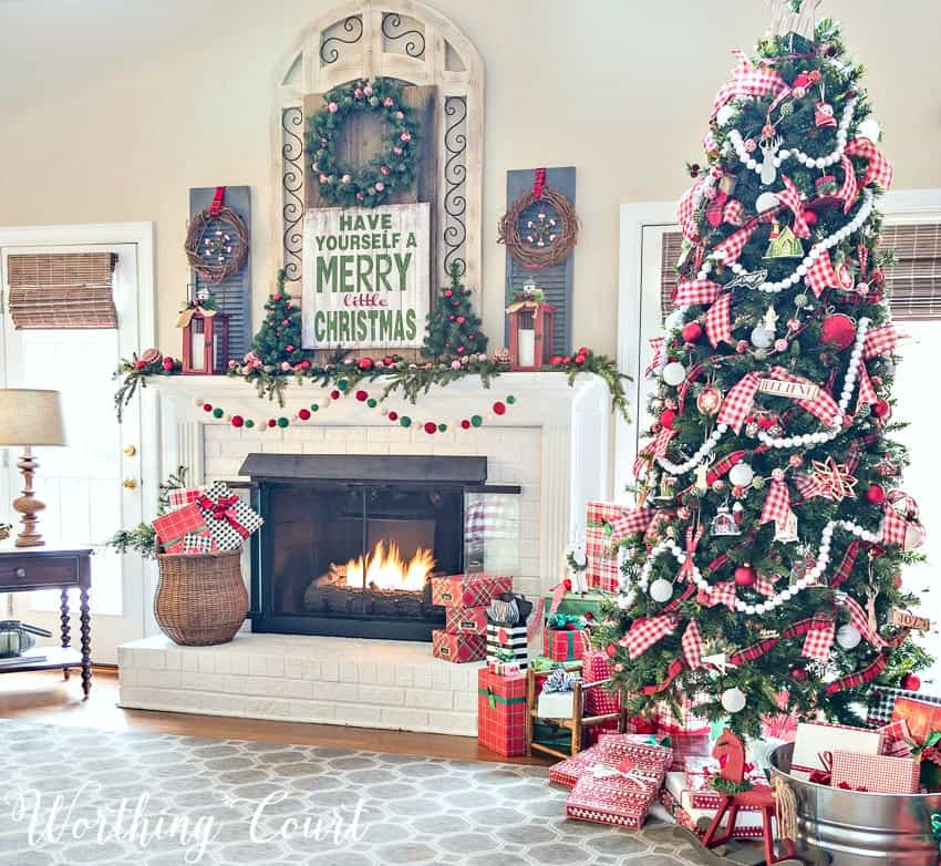 Festive Christmas colors on the mantel and a large Christmas tree beside the fireplace.