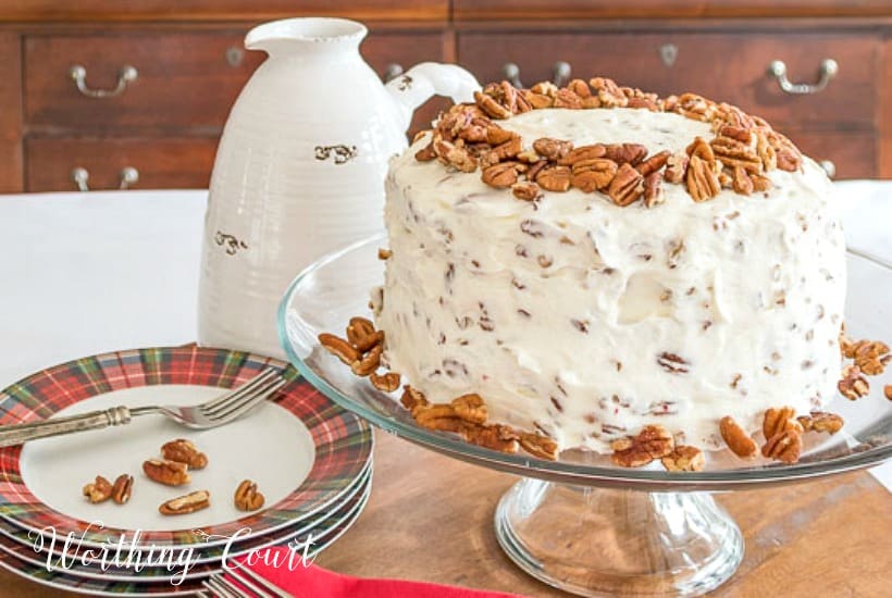 A red velvet cake decorated on a clear plate stand with plaid plates beside it.