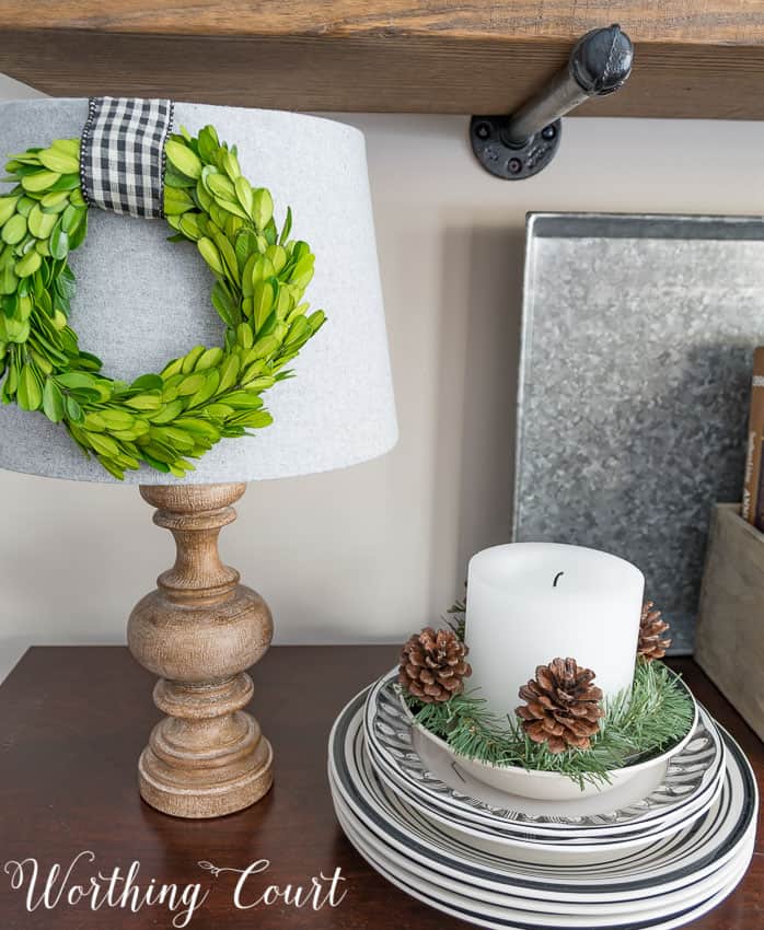 A white candle with pine cones sitting in a bowl that is on plates.