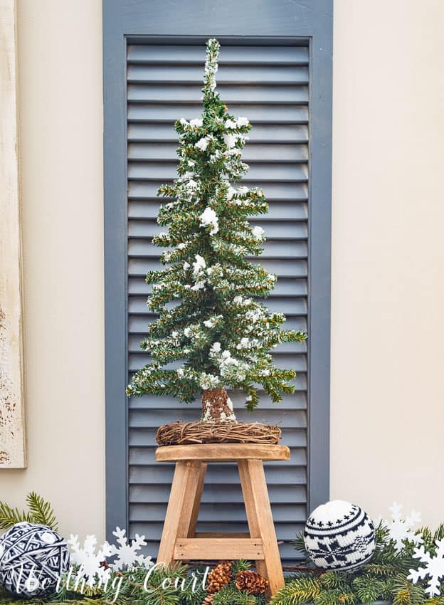 A small Christmas tree on a wooden stool with a shutter background.