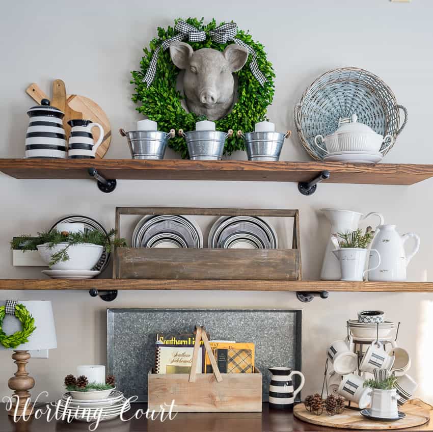 Open shelves with a rustic wooden box, plates, a green wreath and cups and saucers.