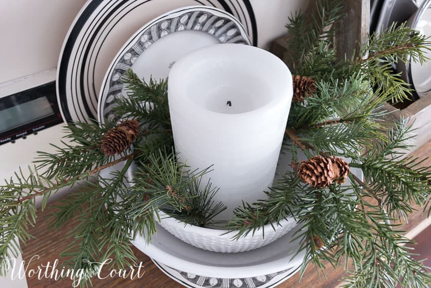 Chunky white candle surrounded with artificial greenery for winter.