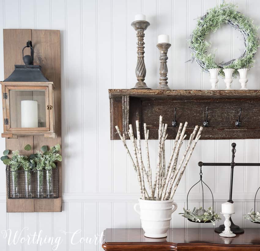 Winter farmhouse dining room decor with candles decorating the sideboard and a wooden shelf with candlesticks on it.