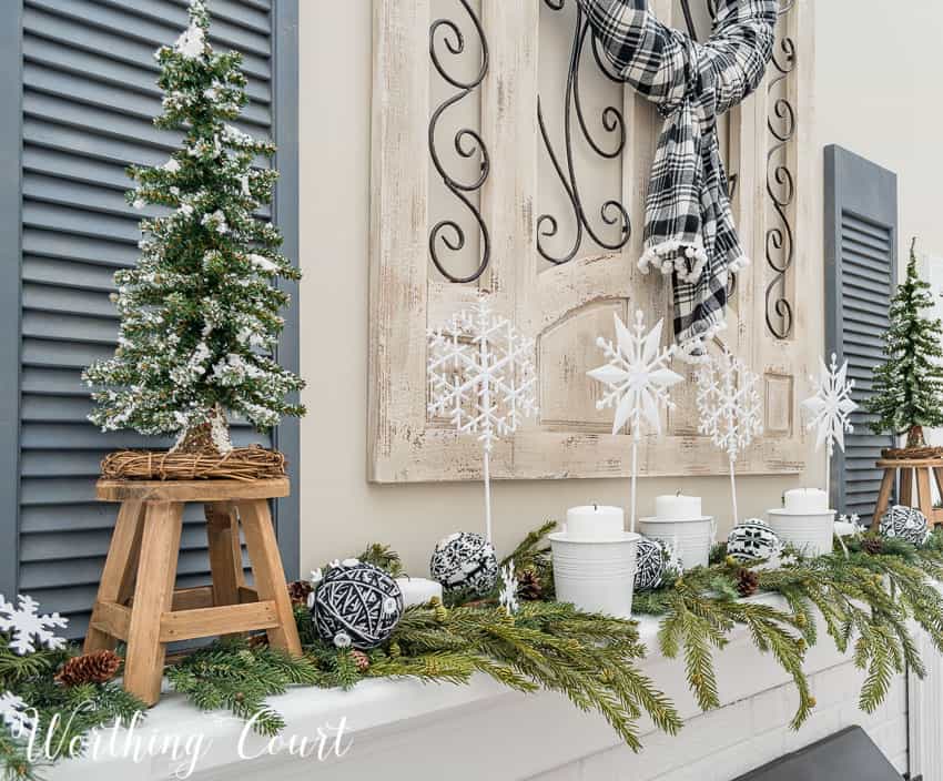 Winter mantel decorated with faux greenery, white candles and diy snowflakes on a stick.