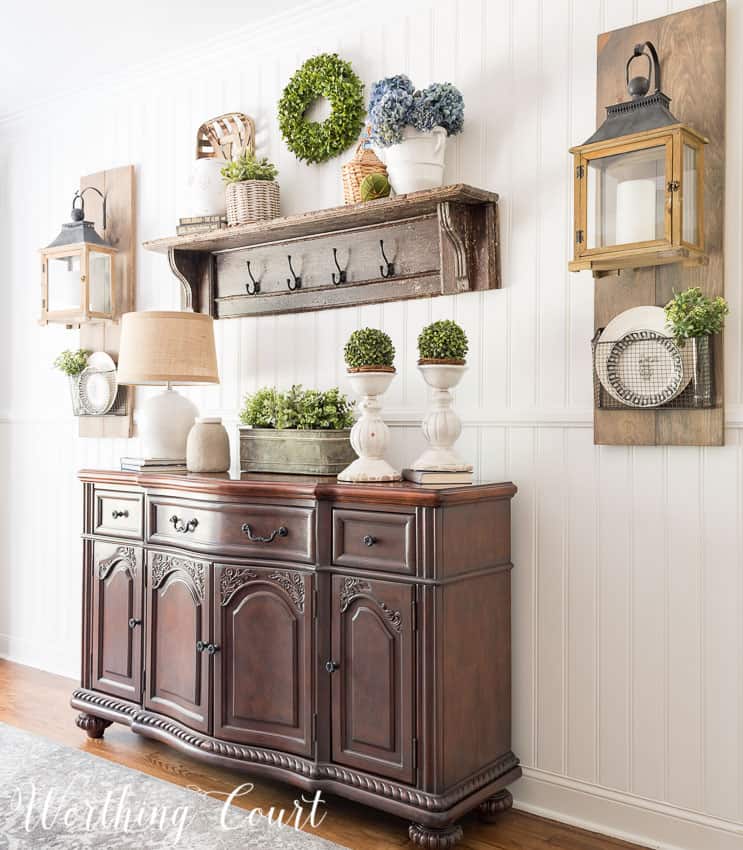A wooden console table with a small wooden shelf above it. All is decorated with greenery and soft florals.