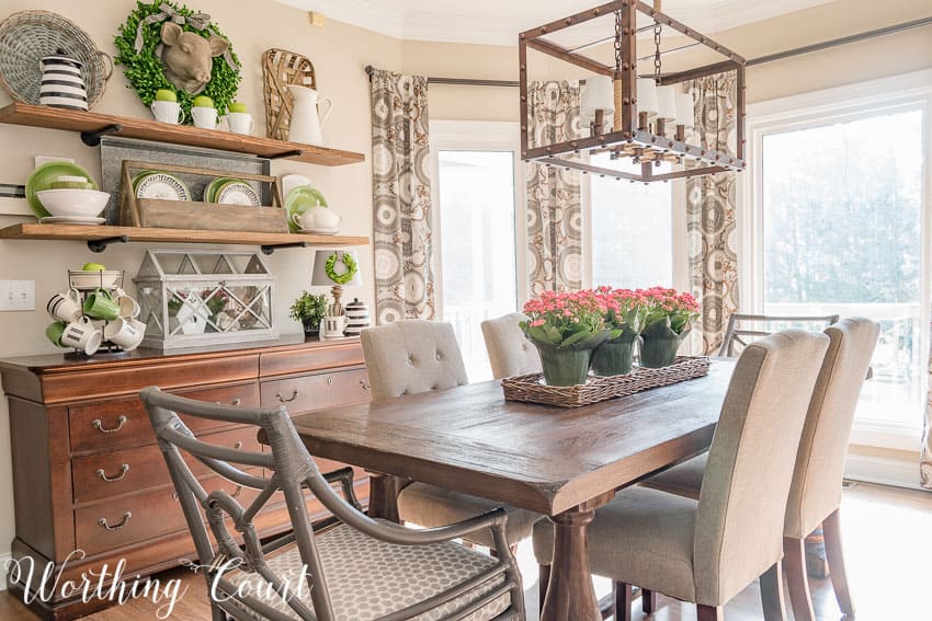 A wooden dining room table with pink flowers as a centerpiece.