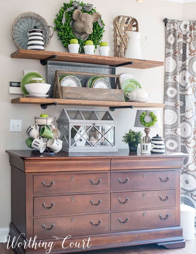 Wooden shelves with tea cups, a wreath, and a geranium all with pops of green.