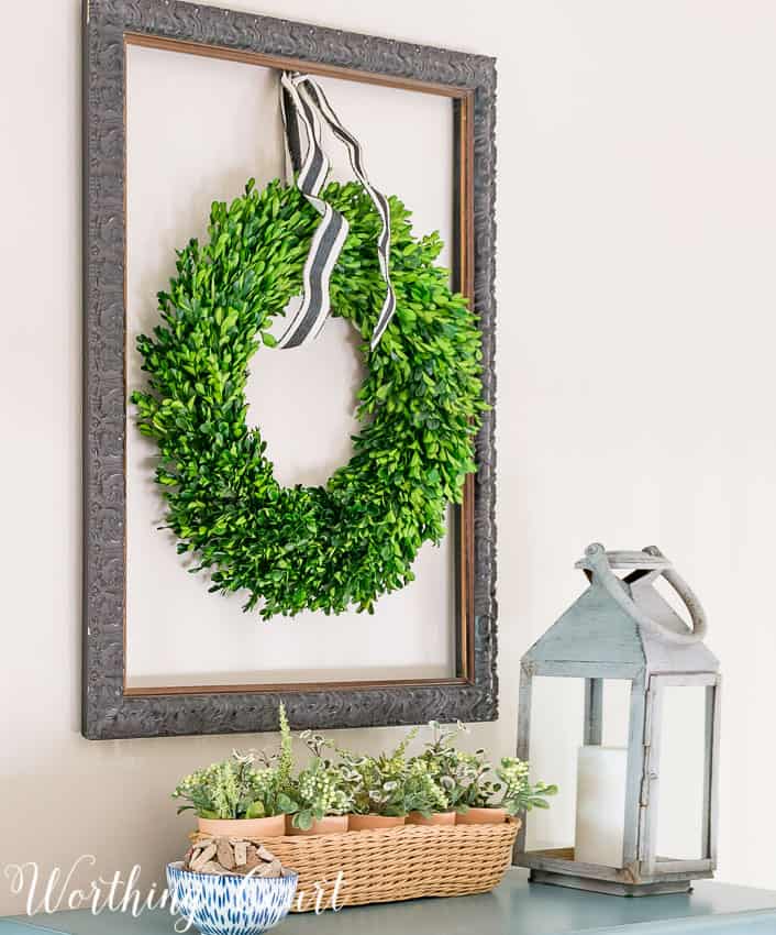 Hang a boxwood wreath inside an old empty picture frame .