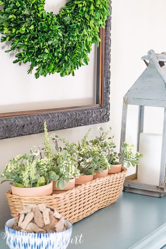 Clay pots from the dollar store placed in a thrifted basket and filled with clippings from artificial greenery bushes on the top of the chest of drawers.