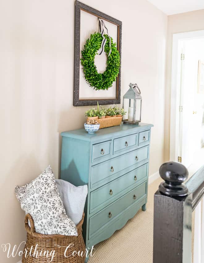 There is a turqoise chest of drawers against the wall in the hallway.