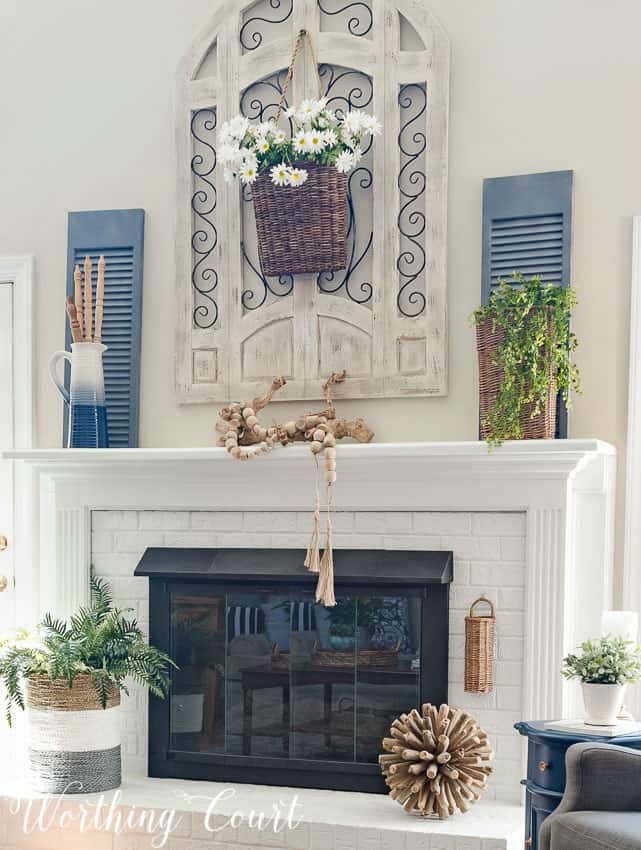 A fireplace mantel with a basket filled with daisies hanging above.